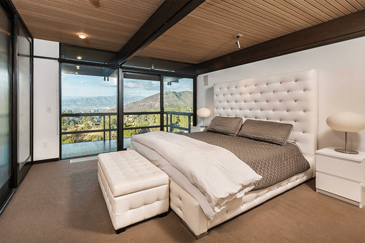 A bedroom with a wooden ceiling and a balcony has a view of the outside.