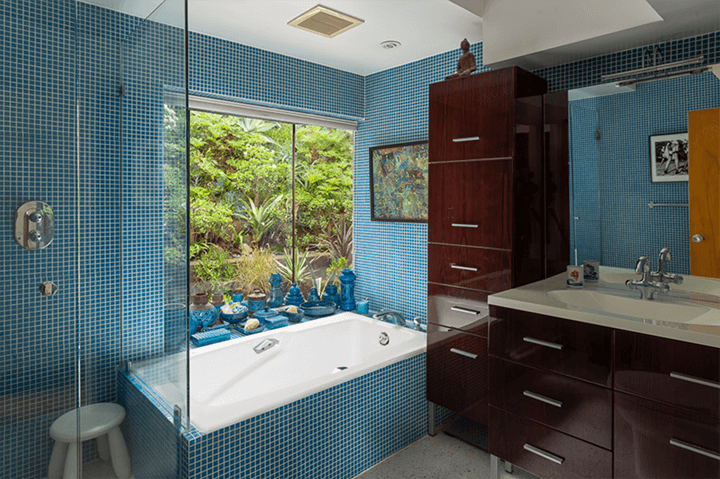 The bathroom has small blue tiles around the bathtub and a black wooden cabinet
