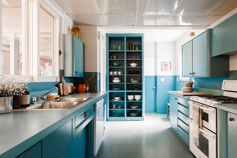 The cabinets of the galley-style kitchen are painted vintage blue. There's a window above the sink looking and a door near the breakfast area looking onto and allowing access to the courtyard.